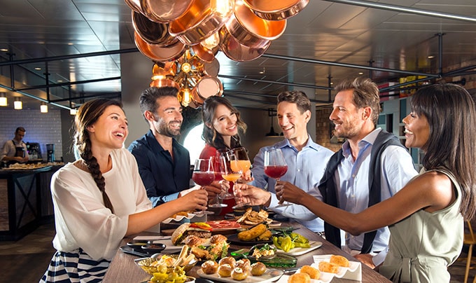 Guests toasting with drinks over gourmet dishes in an elegant onboard dining area | MSC Cruises